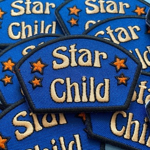 Op de afbeelding: Close-up van verschillende blauwe stoffen patches met de tekst "Star Child" geborduurd in wit en omringd door kleine oranje sterren.