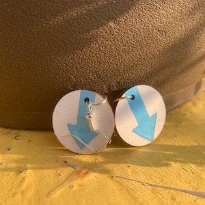 May include: A pair of earrings with a white background and a blue downward arrow painted on each earring.