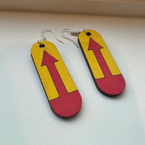 May include: A pair of earrings with a yellow and red arrow design. The earrings are made of wood and have a simple, modern style.