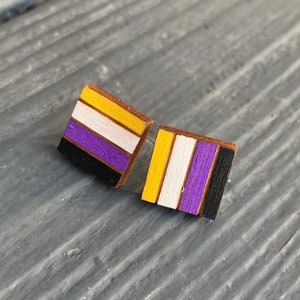 Könnte beinhalten: Ein Paar kleine quadratische Holzohrringe mit den Farben der Non-Binary-Pride-Flagge: Gelb, Weiß, Lila und Schwarz.
