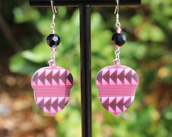 May include: A pair of dangle earrings featuring flat, acorn-shaped charms with a pink and dark brown geometric triangle pattern. Each earring is suspended from a silver-toned hook by a small pink bead and a larger, faceted black bead.