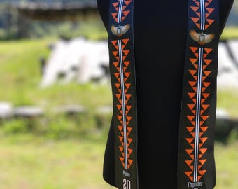 May include: Black graduation sash with orange and white geometric patterns and an eagle emblem. The sash has the text "Pomo 20" and "Thunder Fox 23" on the ends, with beaded tassels.