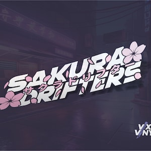 May include: White vinyl decal with the text "SAKURA DRIFTERS" in a stylised font with Japanese characters that read "サクラドリフターズ". The decal is decorated with pink cherry blossoms.