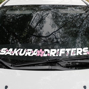 May include: White car windshield with a white vinyl decal that reads "SAKURA DRIFTERS" with pink cherry blossoms.