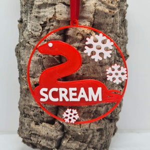 May include: Red Christmas bauble featuring a white snake and the word "SCREAM" in white. The bauble is decorated with white snowflakes.