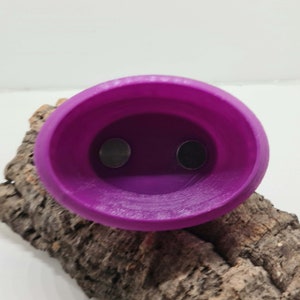 May include: A purple plastic planter with two holes in the bottom. The planter is sitting on a piece of bark.