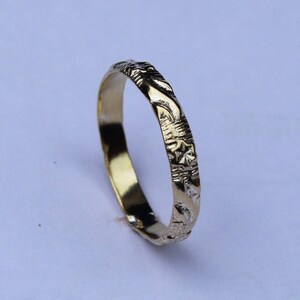 Puede incluir: Un anillo de banda de oro con un diseño detallado y texturizado.