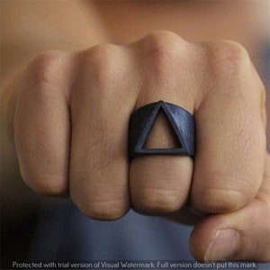 May include: A black ring with a triangular cutout design. The ring is worn on a person's finger.