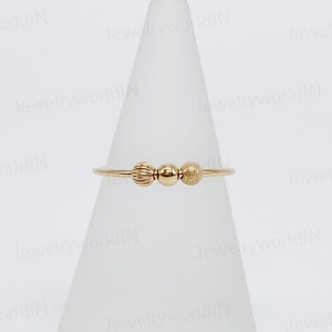 Peut inclure: Une bague en or avec trois perles rondes. Les perles sont de tailles et de textures différentes. La bague est sur un présentoir blanc.