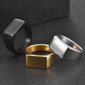 Puede incluir: Tres anillos de forma cuadrada en negro, dorado y plateado. Los anillos están hechos de acero inoxidable y tienen una superficie plana y pulida.