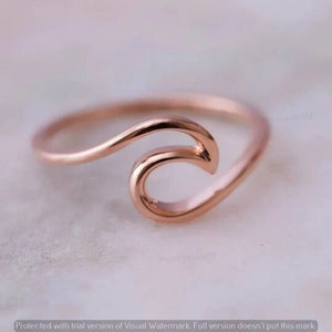 Könnte beinhalten: Ein Wellenring aus Roségold. Der Ring besteht aus einem dünnen Metallband mit einem Wellendesign.
