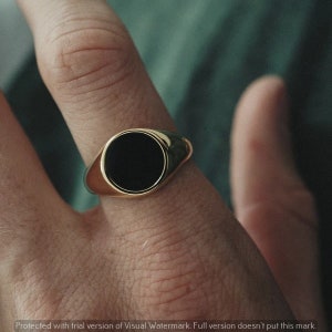 Puede incluir: Un anillo de sello de oro con una piedra ovalada negra.