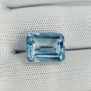 Puede incluir: Una piedra preciosa de aguamarina azul claro con un corte rectangular esmeralda.