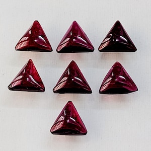 May include: Seven triangular red gemstone cabochons, each with a faceted surface, arranged in a symmetrical pattern on a white background.