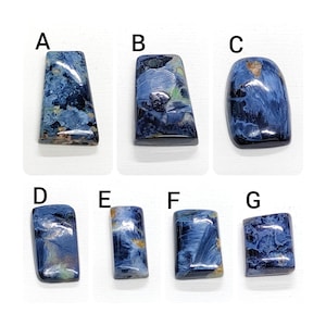 May include: Seven blue and gray tiger's eye cabochons, labeled A through G, are arranged in two rows on a white surface.