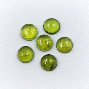 Op de afbeelding: Zes ronde, groene edelstenen met een gladde, gepolijste afwerking. De edelstenen zijn in een cluster op een witte achtergrond gerangschikt.