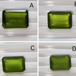 May include: Four green gemstones, labeled A, B, C, and D, are displayed on a white surface with a striped pattern. The gemstones are all cut in a rectangular shape with beveled edges.
