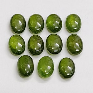 以下が含まれることがあります： 白い表面に3列に並んだ、12個の楕円形の緑色の宝石。おそらくペリドットです。