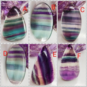 Può includere: Sei cabochon di fluorite di diverse forme e dimensioni, con un arcobaleno di colori tra cui viola, verde, blu e bianco. I cabochon sono disposti in due file di tre, con ogni cabochon etichettato con una lettera dalla A alla F.