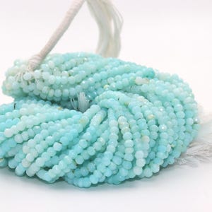 May include: A bundle of light blue faceted gemstone beads. The beads are strung together, forming multiple strands. A white tassel is attached to the top of the bundle. The beads have a slight sparkle and are a soft, pastel color.