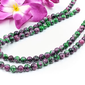 Peut inclure: Un brin de perles de pierres précieuses vertes et roses. Les perles sont rondes et ont un aspect marbré.