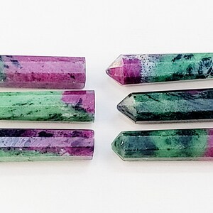 Może przedstawiać: Sześć zielonych i różowych punktów kamieni szlachetnych, znanych również jako rubelit, ułożonych jest w dwóch rzędach po trzy. Punkty są wypolerowane i mają gładką, fasetowaną powierzchnię.