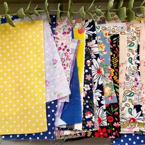 May include: A collection of rectangular fabric scraps featuring various patterns including yellow with white polka dots, floral prints, paisley designs, and solid colours. The assortment includes diverse textiles with white, blue, yellow, red, and green hues arranged in a layered stack.