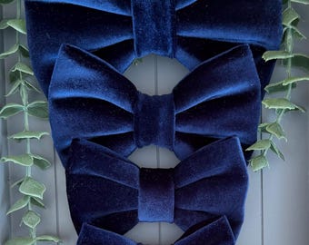 May include: A set of four navy blue velvet bow ties arranged in a vertical column from largest to smallest. Each bow tie features a soft, plush texture with a central fabric knot, showcasing a deep, rich blue color and a classic, symmetrical shape.