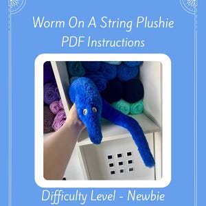 May include: A blue plush worm with white eyes, held in front of a shelf filled with yarn. The image includes the text "Worm On A String Plushie PDF Instructions." The difficulty level is marked as "Newbie." The text "Pattern Only - Not a Physical Item" is also present.