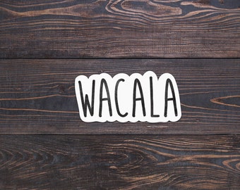 May include: White sticker with the word "WACALA" written in black on a dark brown wooden background.