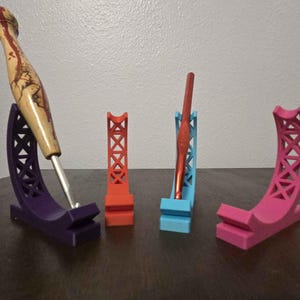 May include: Four colorful crochet hook holders in purple, red, blue, and pink. The purple holder has a wooden crochet hook with a decorative handle. The other holders are empty and have a geometric design.