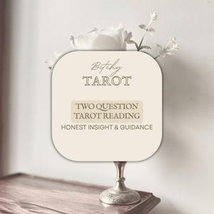 Könnte beinhalten: Eine beige Karte mit dem Text "Bitchy Tarot" und "Two Question Tarot Reading: Honest Insight & Guidance." Die Karte befindet sich auf einem silbernen Ständer, mit weißen Blumen im Hintergrund.