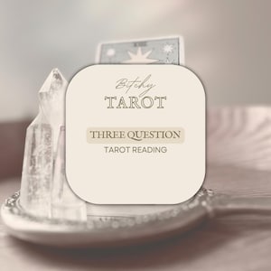 May include: A light beige graphic with the text "Bitchy Tarot" and "Three Question Tarot Reading". The graphic is set on a silver tray with two clear quartz crystals and a tarot card.