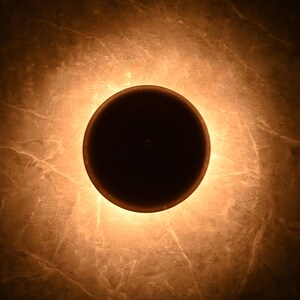 May include: A round, black, light fixture with a warm, yellow glow emanating from the edges.