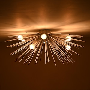 May include: A silver ceiling light fixture with multiple thin metal rods radiating outwards from a central hub. The light fixture has six round light bulbs.