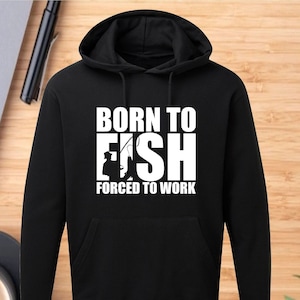 May include: Black hooded sweatshirt with white text that reads "Born to Fish Forced to Work". The text is in a bold, blocky font. A silhouette of a person fishing is incorporated into the word "Fish".