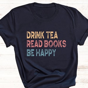 May include: A navy blue t-shirt with the text "Drink Tea Read Books Be Happy" in a vintage style font with colourful accents.