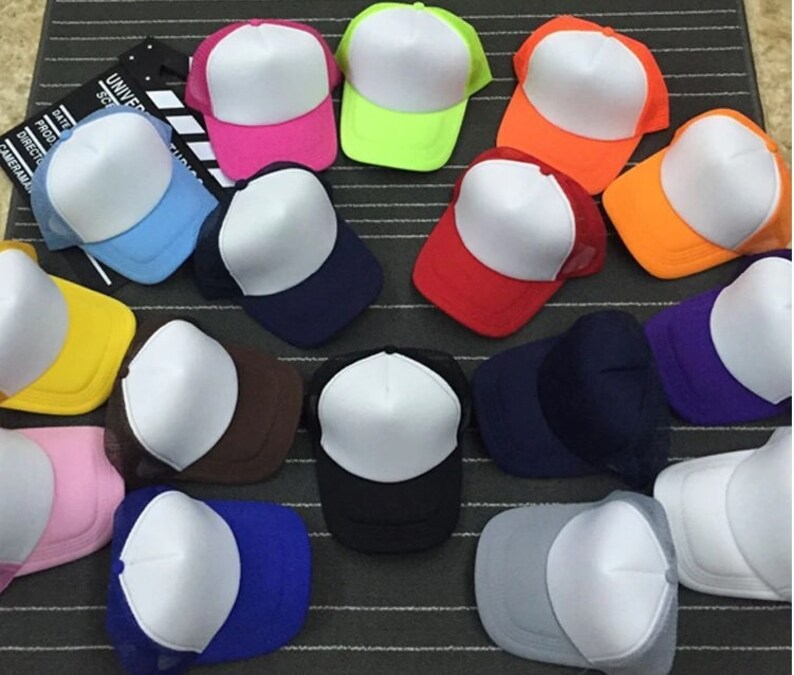 May include: A collection of 15 blank trucker hats in various colors, including red, blue, yellow, pink, orange, green, purple, brown, and black. The hats have a white front panel and a mesh back.