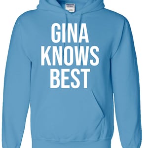 Peut inclure: Un sweat à capuche bleu clair avec le texte "GINA KNOWS BEST" imprimé en blanc sur le devant.