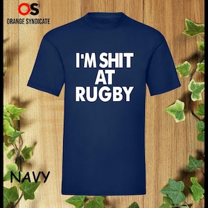 Puede incluir: Una camiseta azul marino con texto blanco que dice "I'M SHIT AT RUGBY".