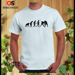 May include: A white t-shirt with a black silhouette of the evolution of man, ending with two men wrestling. The text "WHITE" is visible in the lower left corner of the image.