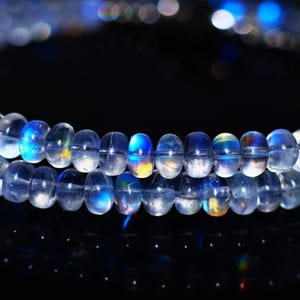 Op de afbeelding: Een close-up van een ketting gemaakt van heldere, iriserende kralen. De kralen hebben een afgeronde vorm en reflecteren blauw, geel en groen licht. De ketting wordt tegen een donkere achtergrond weergegeven.