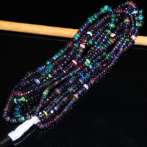 May include: Strands of dark, iridescent beads with a variety of colors, including green, blue, red, and pink. The beads are small and round, strung together to form multiple strands. The beads are on a black surface.