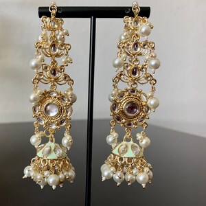 May include: A pair of long, gold-tone earrings with multiple tiers of white pearls and clear rhinestones. The bottom tier features a round, green-enameled pendant with clear rhinestones.