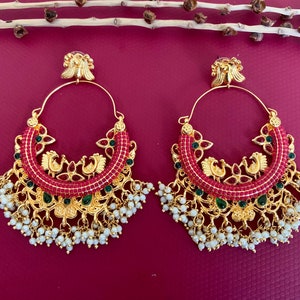May include: A pair of gold hoop earrings with a red and green design. The earrings feature a peacock design and are adorned with white pearls.
