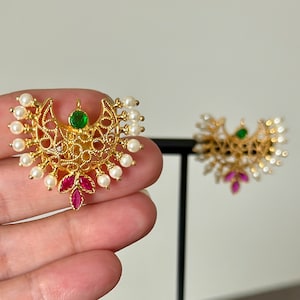 May include: A pair of gold earrings with a crescent moon design, featuring white pearls, green and pink gemstones.