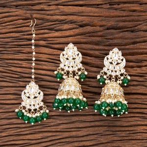 May include: A set of gold-tone earrings and a matching nose ring with green and white beads. The earrings feature a teardrop shape with a decorative design.