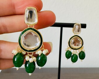 May include: A pair of gold earrings with green and white stones. The earrings have a round, clear stone in the center, surrounded by a green border. The stones are attached to a gold chain with small white pearls and green teardrop-shaped stones.