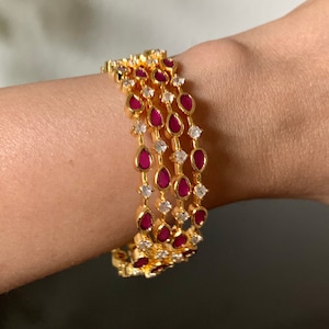 May include: Four gold bangles with a row of teardrop-shaped ruby red stones and clear cubic zirconia stones.