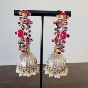 May include: A pair of silver-toned chandelier earrings with red and gold accents. The earrings feature a cluster of red gemstones and a silver bell-shaped bottom with a gold trim and small white pearl dangles.
